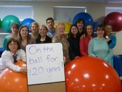 Group of staff celebrating 120th Birthday of Cotting and Pride Day with a sign and balloons